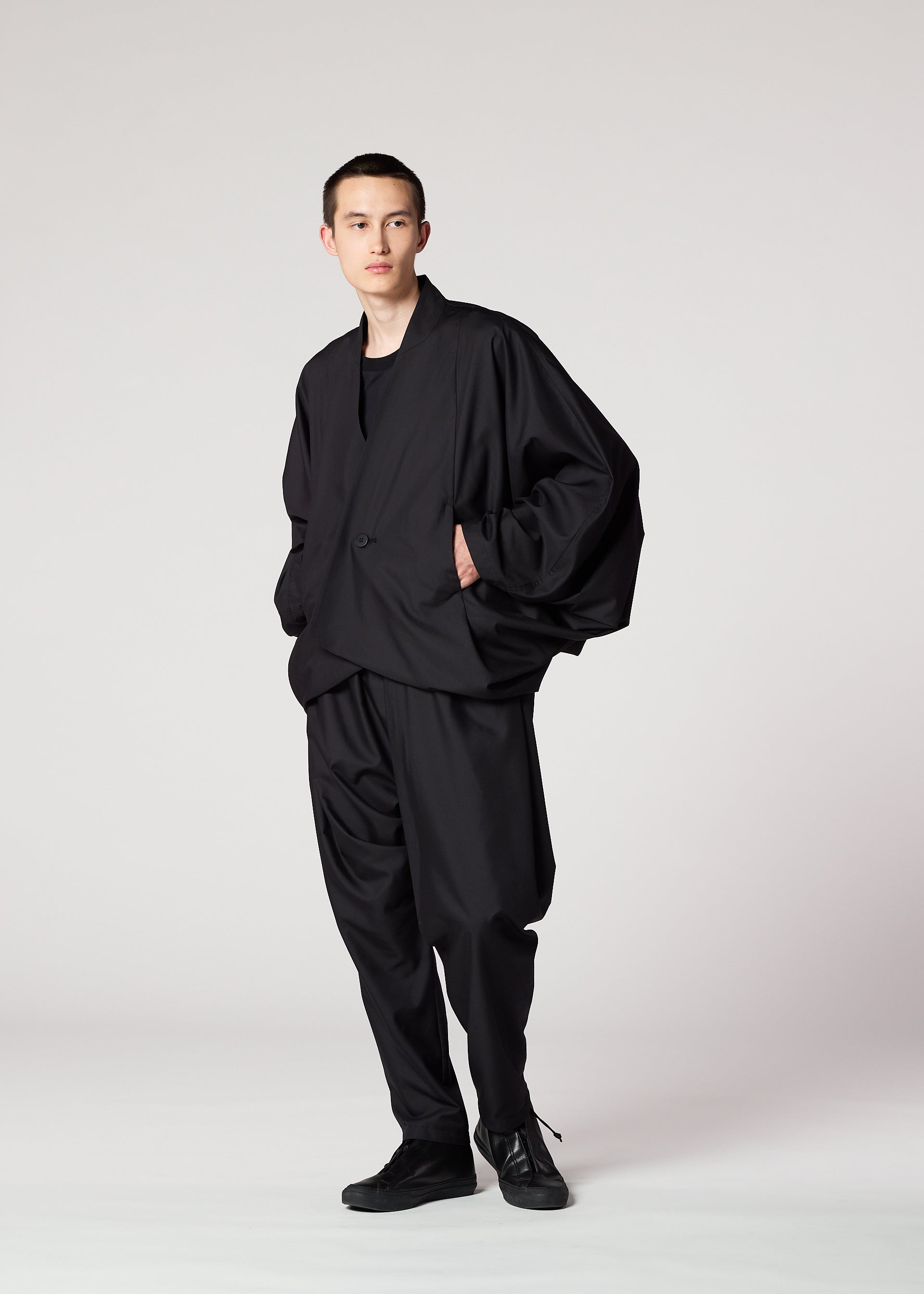 Zoomed view Against a plain light background, a person wears IM MEN's SWING BLACK lightweight pants with a loose silhouette, paired with a black shirt, an oversized black jacket, and black shoes. Their hands are in their pockets as they look slightly to the side.