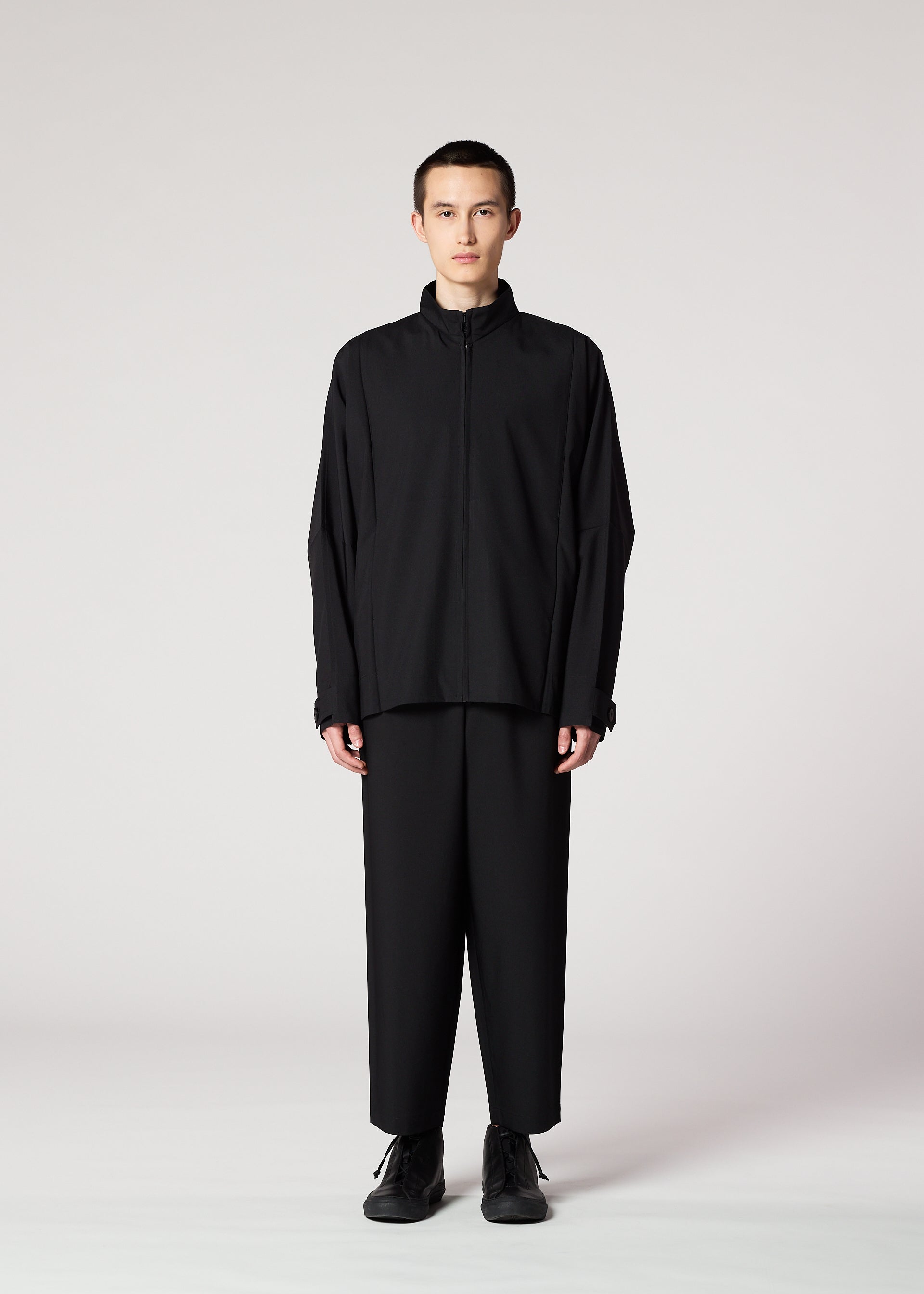 Zoomed view A person stands facing forward, wearing IM MEN's FLAT BLACK zip-up jacket and wide wrinkle-resistant pants with black shoes, set against a plain light gray background.