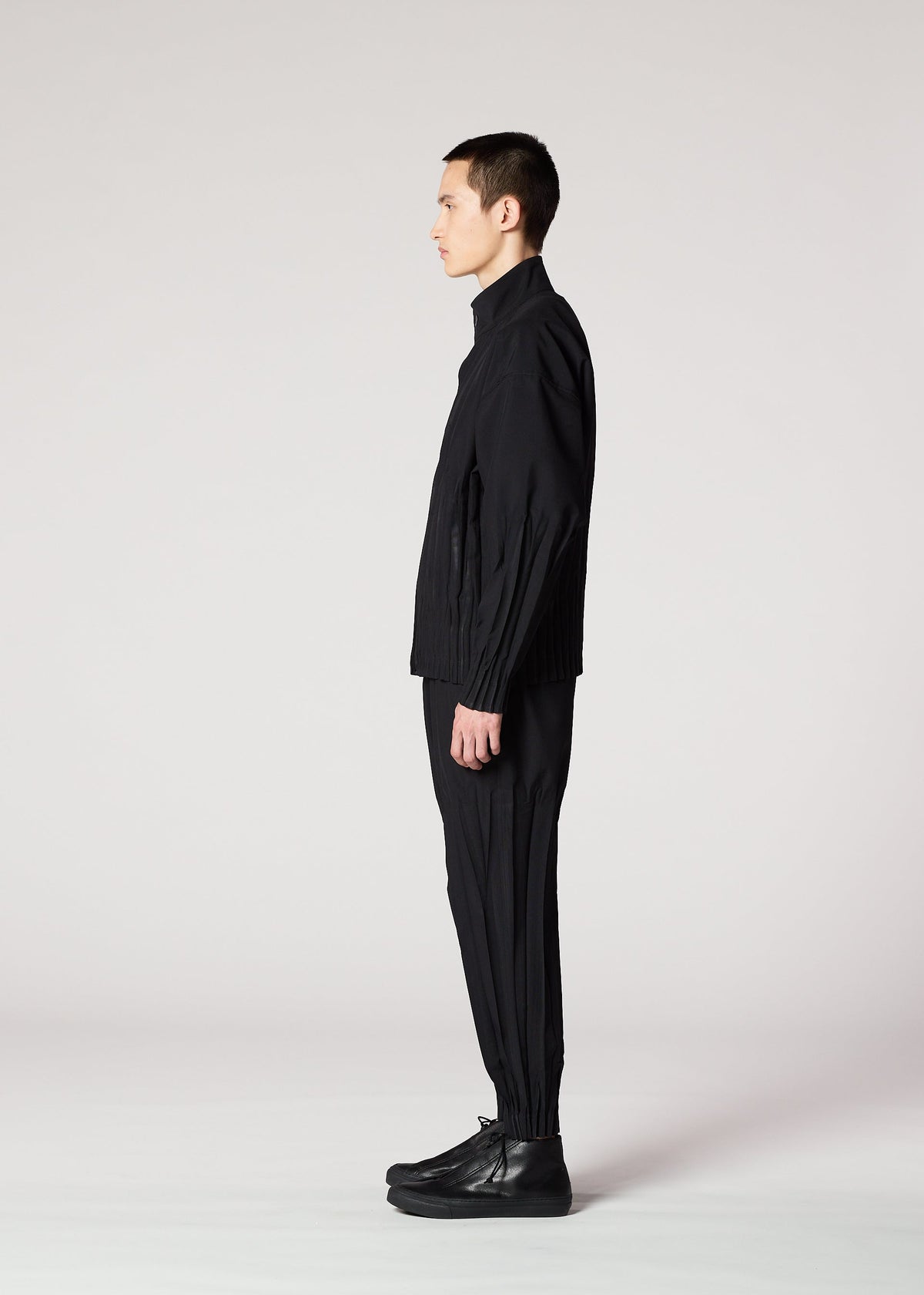 A person with short dark hair stands in profile against a plain light background, wearing IM MEN's WAFT BLACK jacket, easy care pants, and black shoes. view 5 of 15