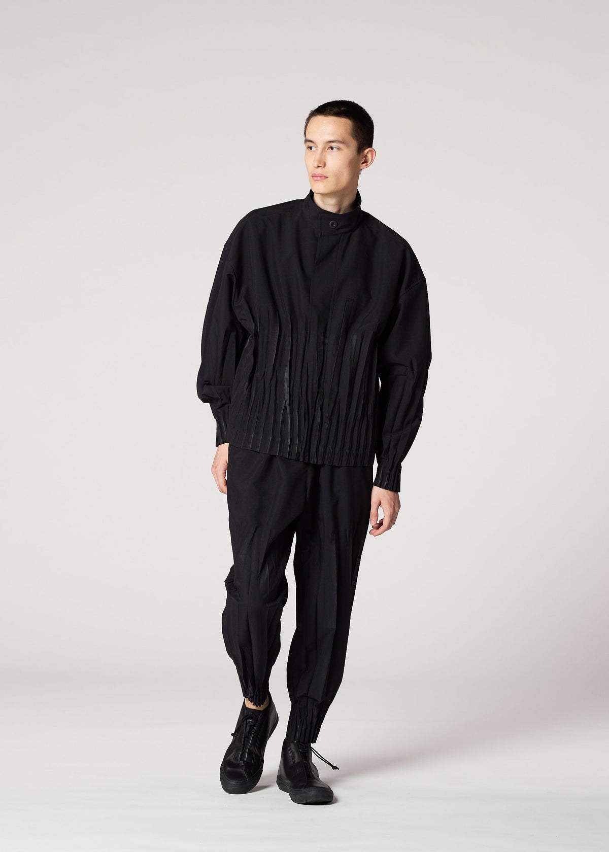 A person stands against a plain white background, wearing the IM MEN WAFT BLACK loose-fitting button-up shirt with pleats and wrinkle-resistant pants with gathered ankles, paired with black shoes. They look slightly to the side. view 7 of 15