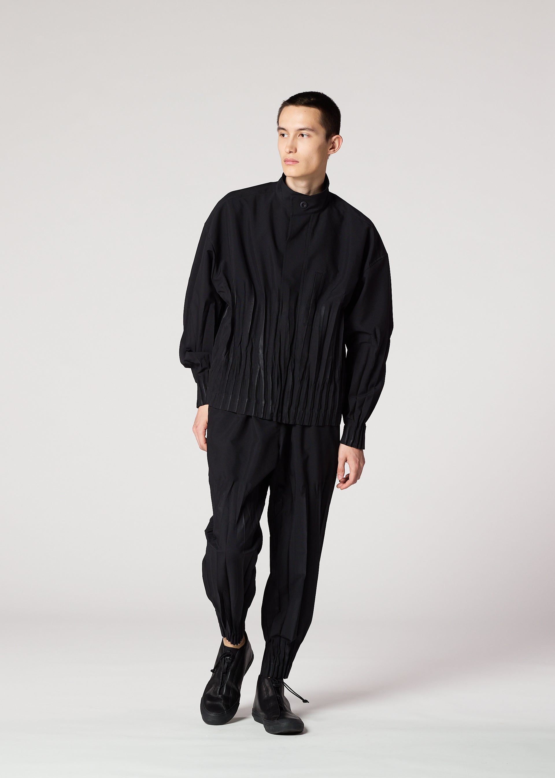 Zoomed view A person stands against a plain white background, wearing the IM MEN WAFT BLACK loose-fitting button-up shirt with pleats and wrinkle-resistant pants with gathered ankles, paired with black shoes. They look slightly to the side.