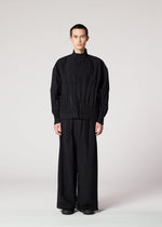 A person stands facing forward, wearing the IM MEN WAFT BLACK loose-fit jacket with pleats and wide-leg, wrinkle-resistant pants, against a plain light grey background.