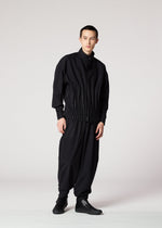 Against a plain background, a person with short hair and a neutral expression wears the IM MEN WAFT BLACK set: a loose pleated jacket and matching wide pants with a linen-like texture, paired with black shoes.