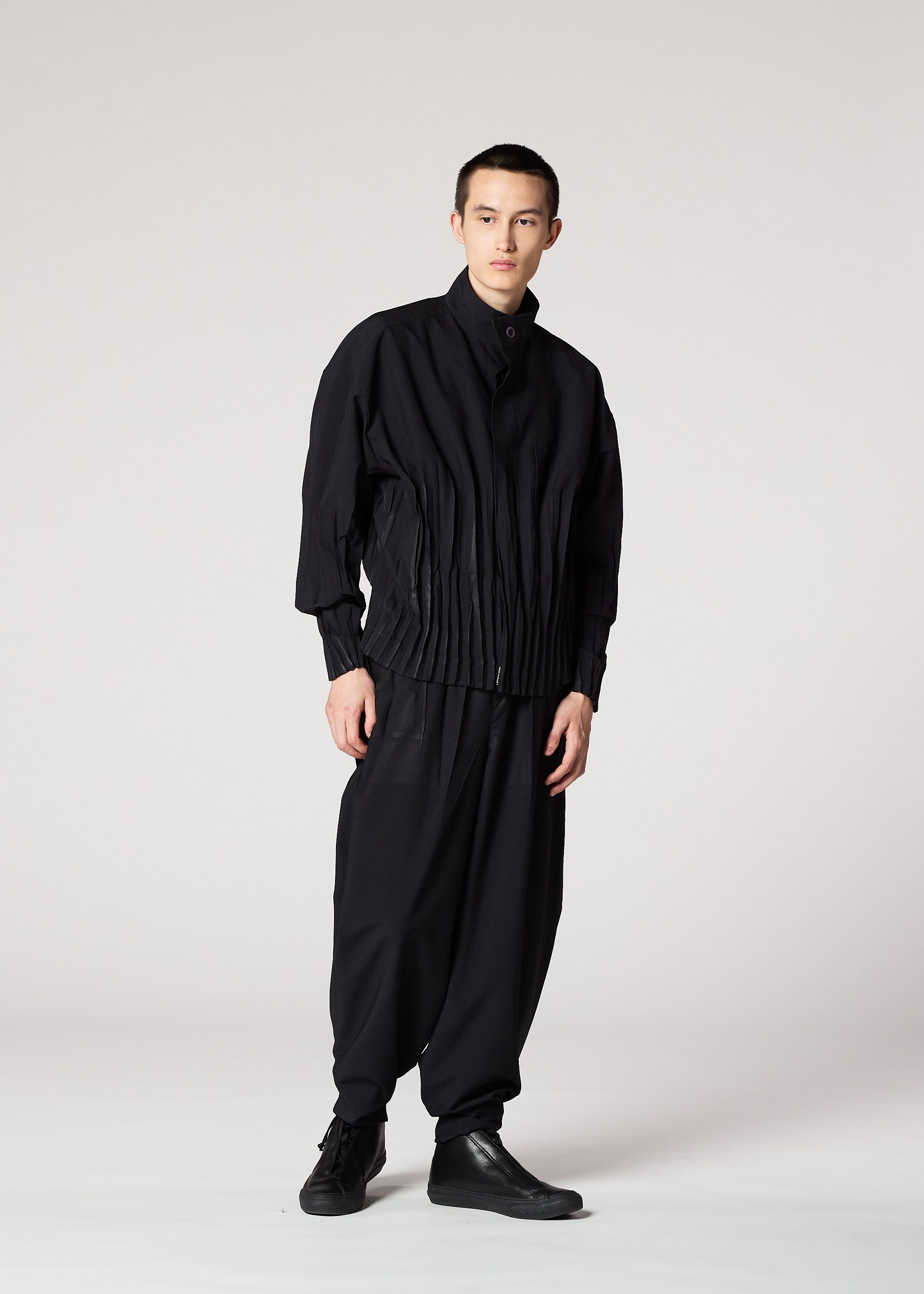 Zoomed view Against a plain background, a person with short hair and a neutral expression wears the IM MEN WAFT BLACK set: a loose pleated jacket and matching wide pants with a linen-like texture, paired with black shoes.
