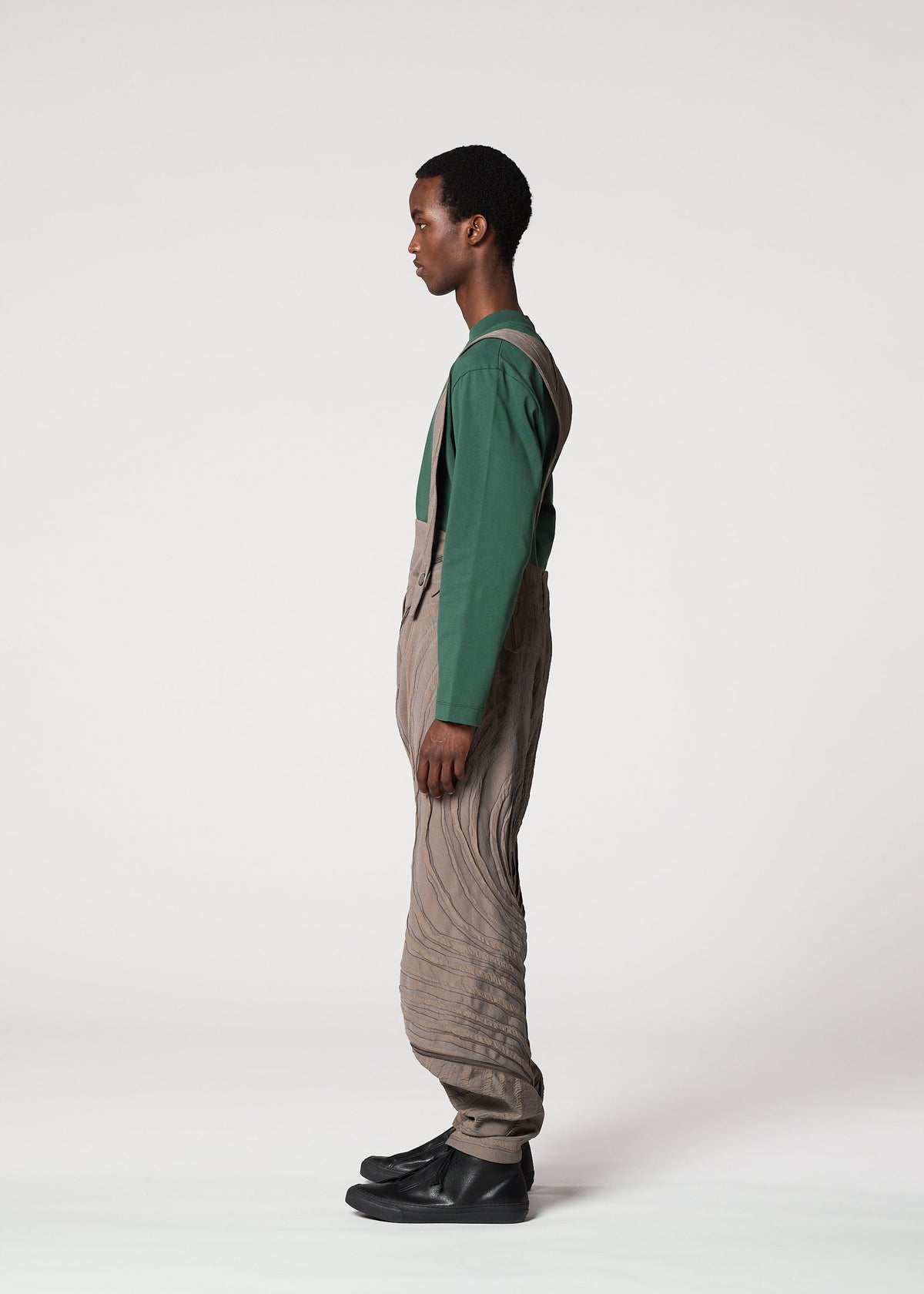 A person stands in profile against a white background, wearing the ENGRAVE long-sleeve shirt and Shoji Kamoda inspired textured tan overalls by IM MEN, paired with black shoes. view 6 of 8