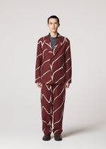 A person faces forward in IM MEN’s EARTH suit—a maroon ensemble with bold wavy white stripes over a dark shirt. Jacquard-textured pants complete the look, while a light background highlights the striking pattern.