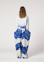 A woman in a long skirt stands gracefully, her style echoing the elegance of IM MEN’s INLAY ceramic-inspired pants.