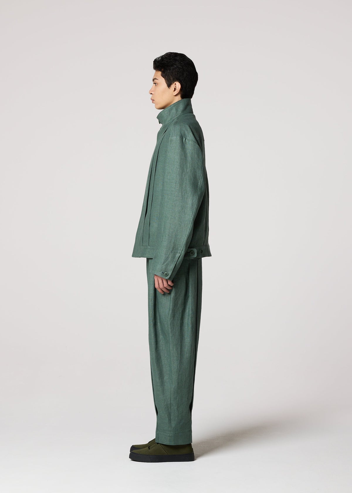 A person stands in profile against a plain light background, wearing the IM MEN TOUGH LINEN suit and matching pants. The natural texture and relaxed fit, paired with dark green shoes, create a durable, effortless look. view 7 of 9