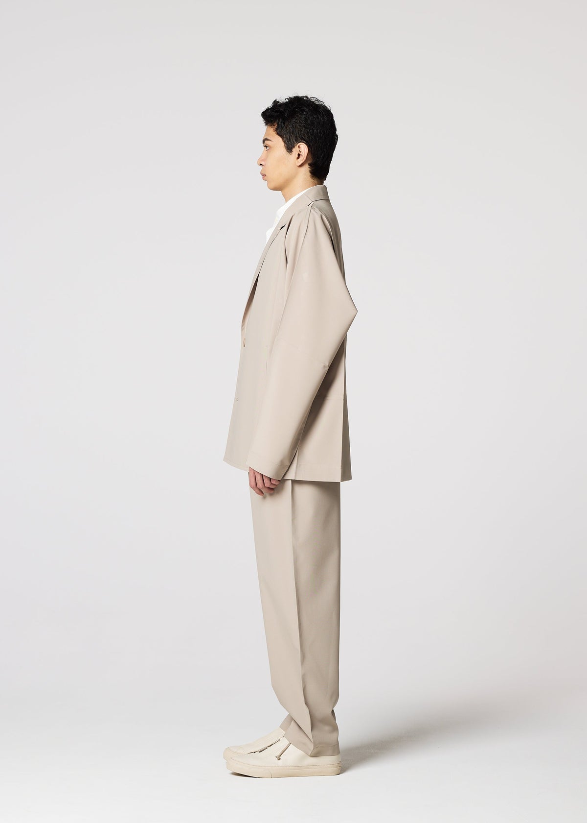A person stands in profile facing left, wearing the IM MEN FLAT oversized beige suit with wrinkle-resistant pants and matching shoes, against a plain white background. view 6 of 8