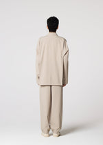 A person with short dark hair, facing away on a plain light background, wears the oversized wrinkle-resistant FLAT suit and pants by IM MEN for easy, compact storage.