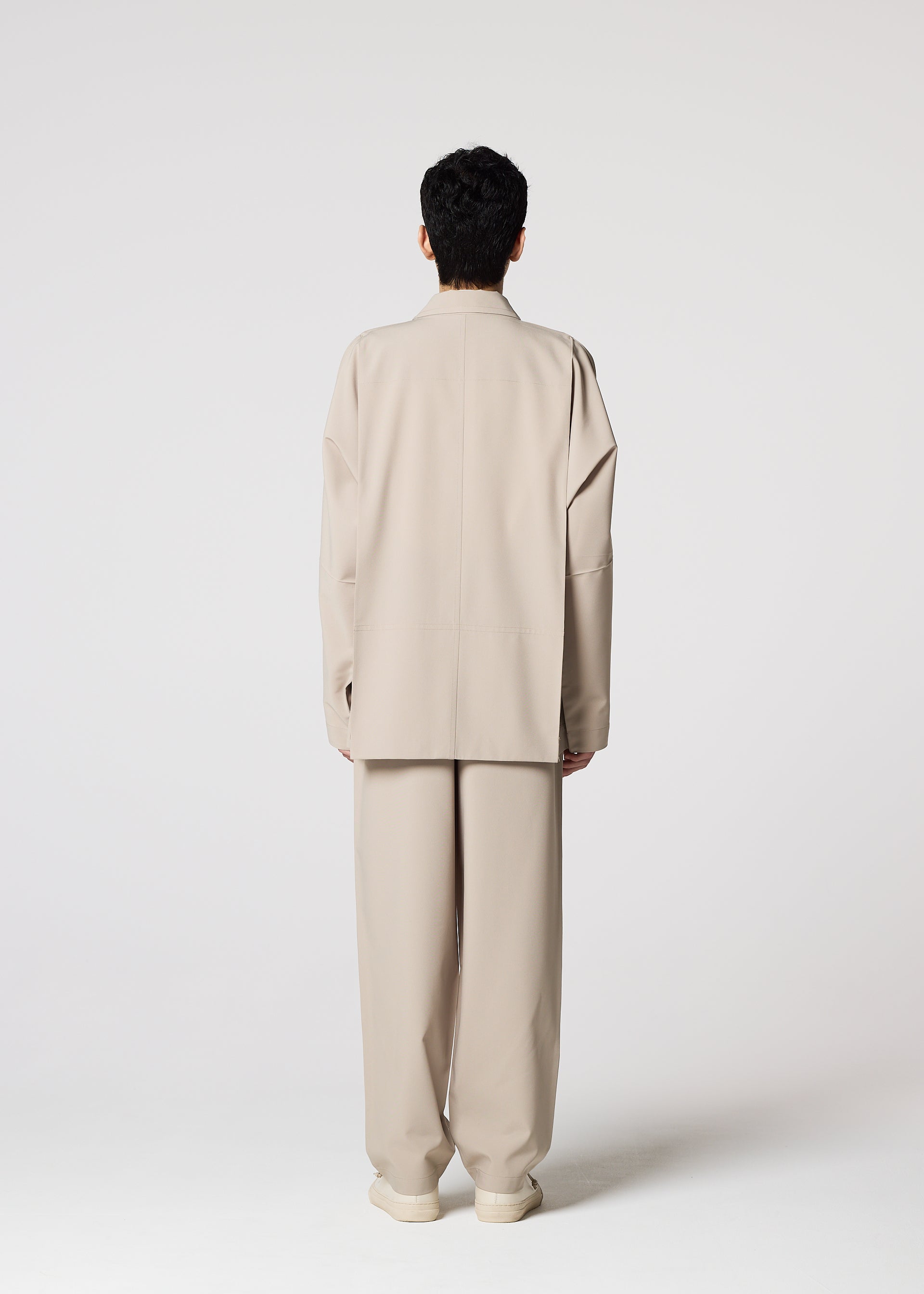 Zoomed view A person with short dark hair, facing away on a plain light background, wears the oversized wrinkle-resistant FLAT suit and pants by IM MEN for easy, compact storage.