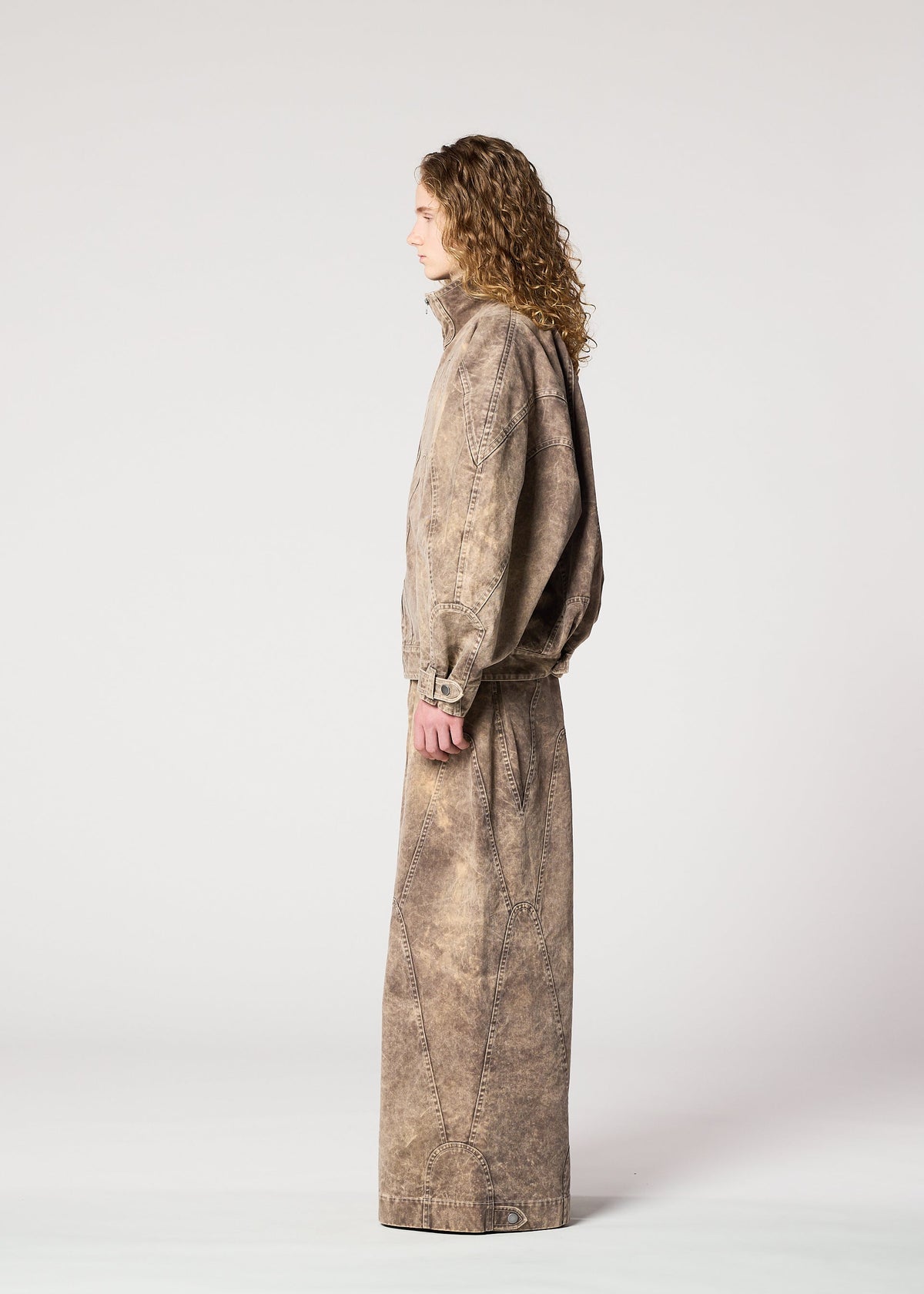 A person with long curly hair in profile wears the IM MEN ELEMENTS loose-fitting, stone-washed brown denim jacket and matching wide pants, both made from thick cotton, against a plain light gray background. view 9 of 11