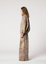 A person with long curly hair in profile wears the IM MEN ELEMENTS loose-fitting, stone-washed brown denim jacket and matching wide pants, both made from thick cotton, against a plain light gray background.