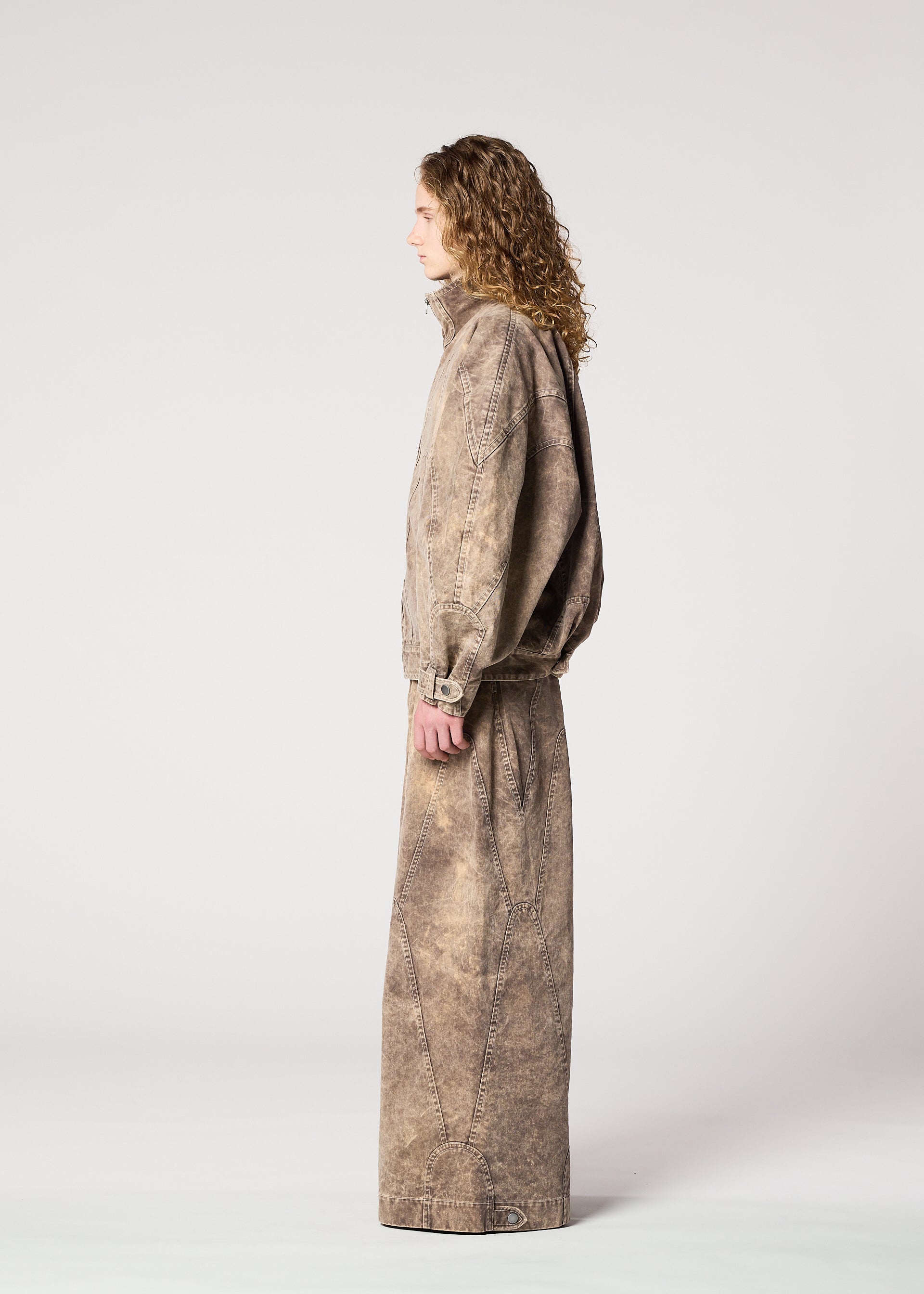 Zoomed view A person with long curly hair in profile wears the IM MEN ELEMENTS loose-fitting, stone-washed brown denim jacket and matching wide pants, both made from thick cotton, against a plain light gray background.