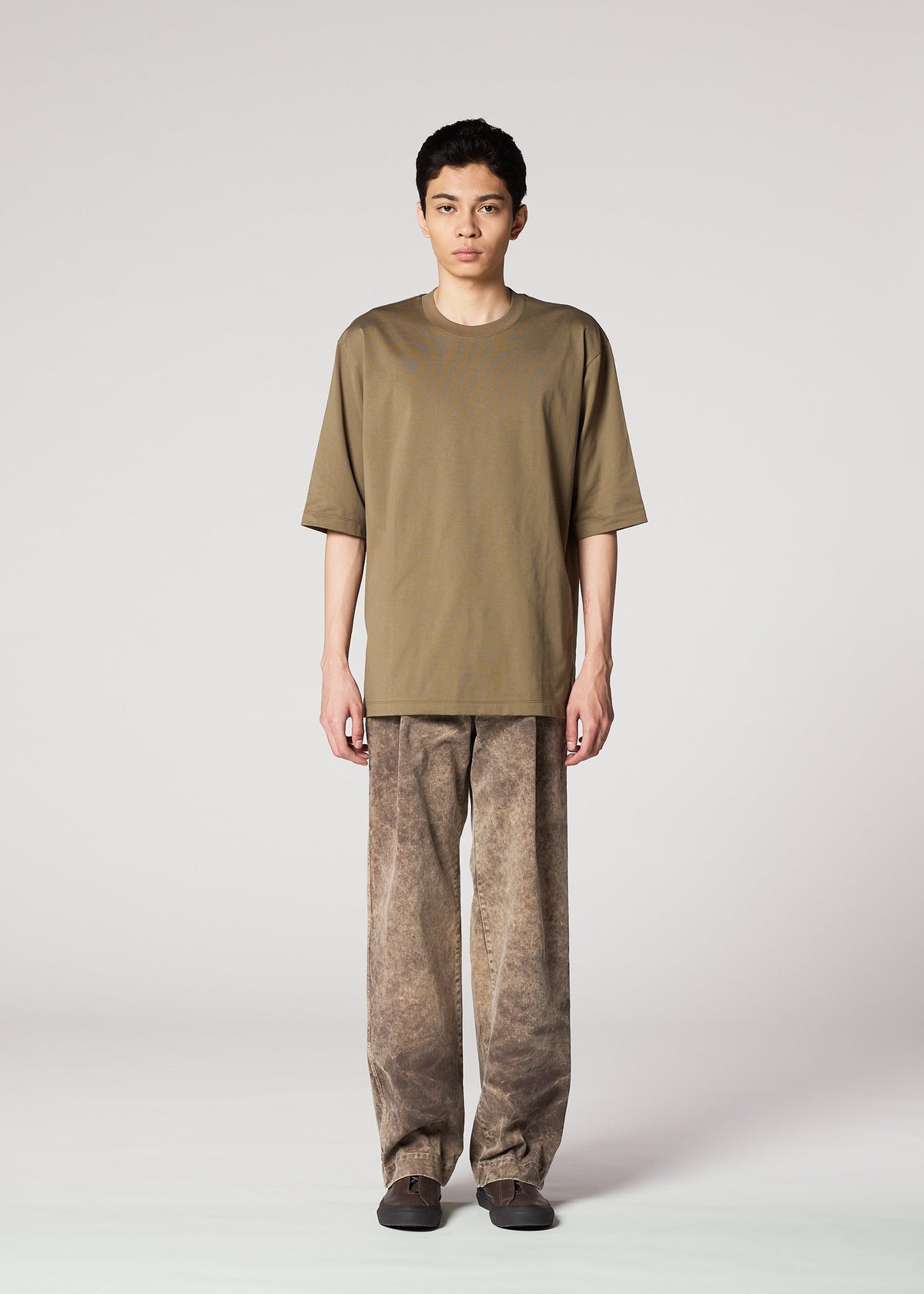 A person stands facing forward in IM MEN’s ELEMENTS olive green T-shirt and ceramic artist-inspired pants with a subtle color-fading effect, paired with dark shoes, set against a plain light grey background. view 5 of 8