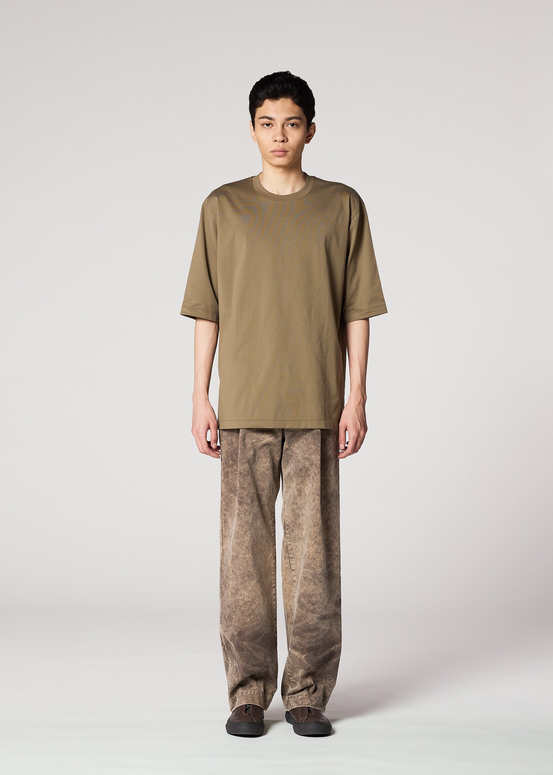 Zoomed view A person stands facing forward in IM MEN’s ELEMENTS olive green T-shirt and ceramic artist-inspired pants with a subtle color-fading effect, paired with dark shoes, set against a plain light grey background.
