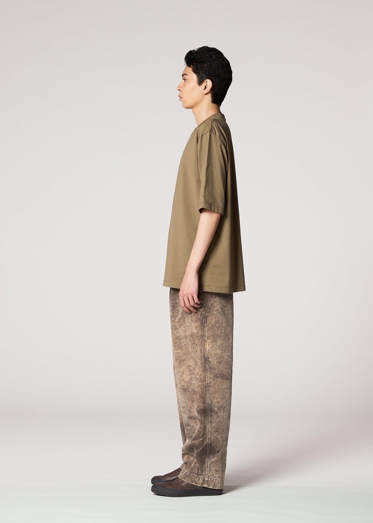 A person in profile facing left wears IM MEN’s ELEMENTS: a loose olive-green shirt and ceramic artist-inspired, brown textured wide-leg pants, paired with dark shoes, set against a plain light gray background. view 6 of 8