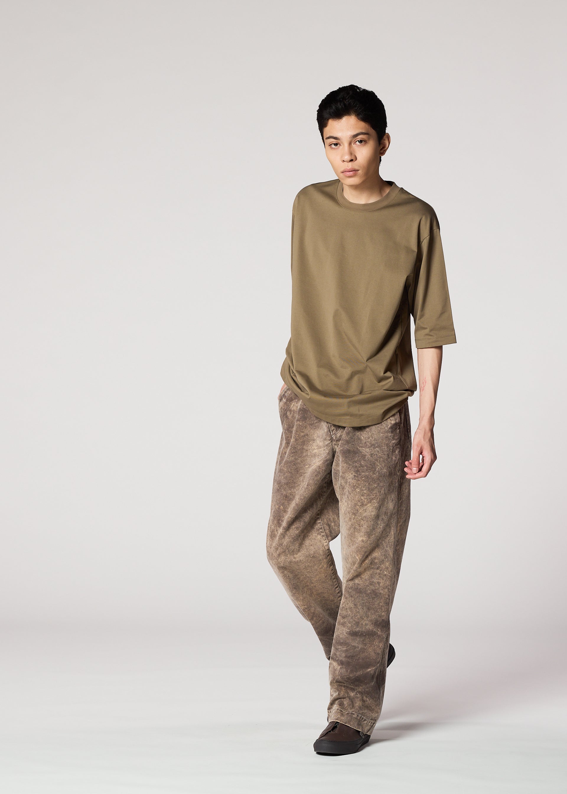 Zoomed view A person with short dark hair wears IM MEN's ELEMENTS: a loose olive t-shirt and wide-legged, faded brown cotton pants, standing against a plain light background.