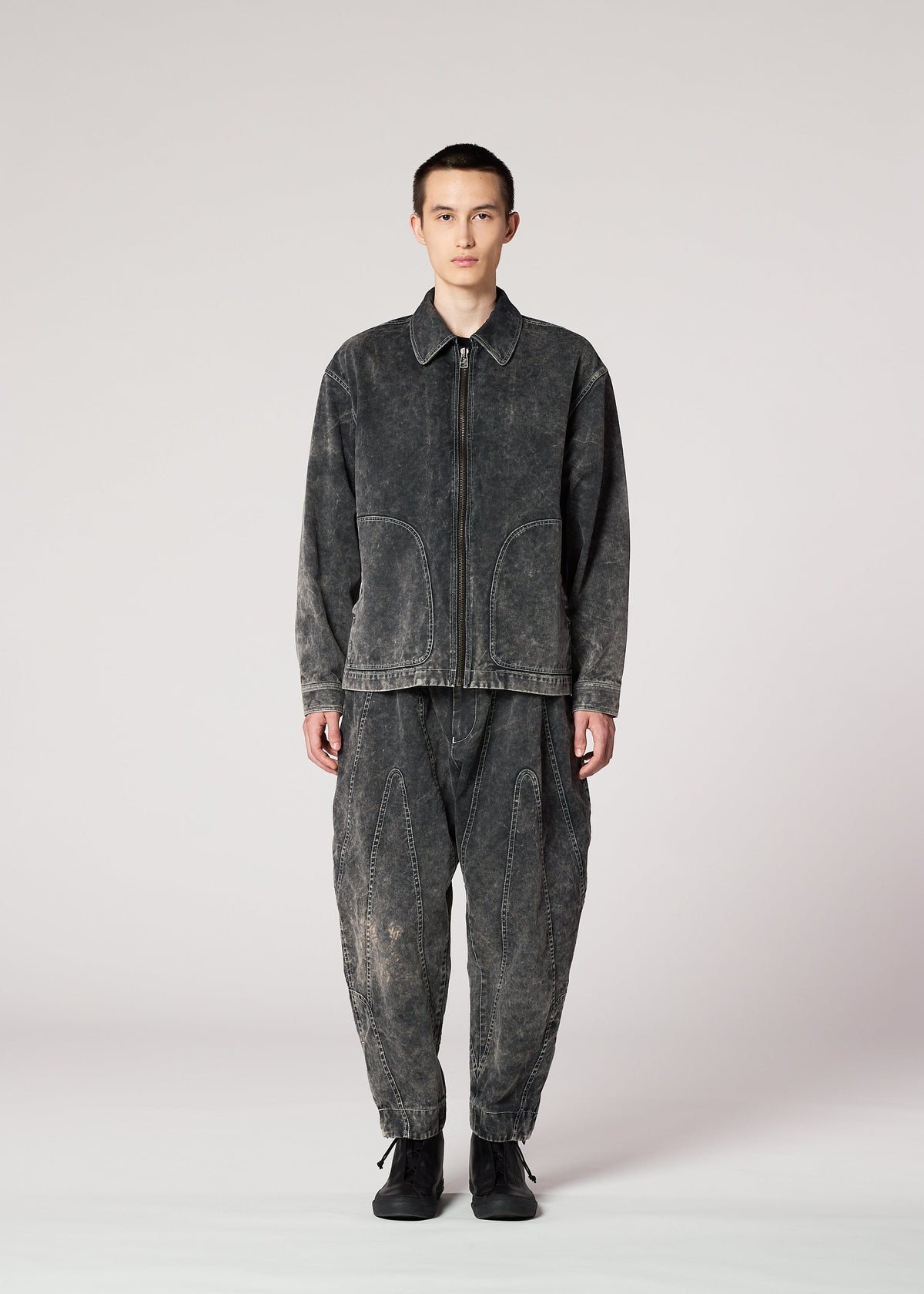 A person faces forward against a plain light grey background, wearing the IM MEN ELEMENTS faded black denim zip-up jacket and matching baggy, irregular-cut thick cotton pants, paired with black shoes. view 5 of 8