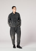 A person wears the IM MEN ELEMENTS dark, washed-out denim jacket and irregular-cut pants with a unique color-fading effect, paired with black ankle boots, standing against a light gray background with hands in pockets.