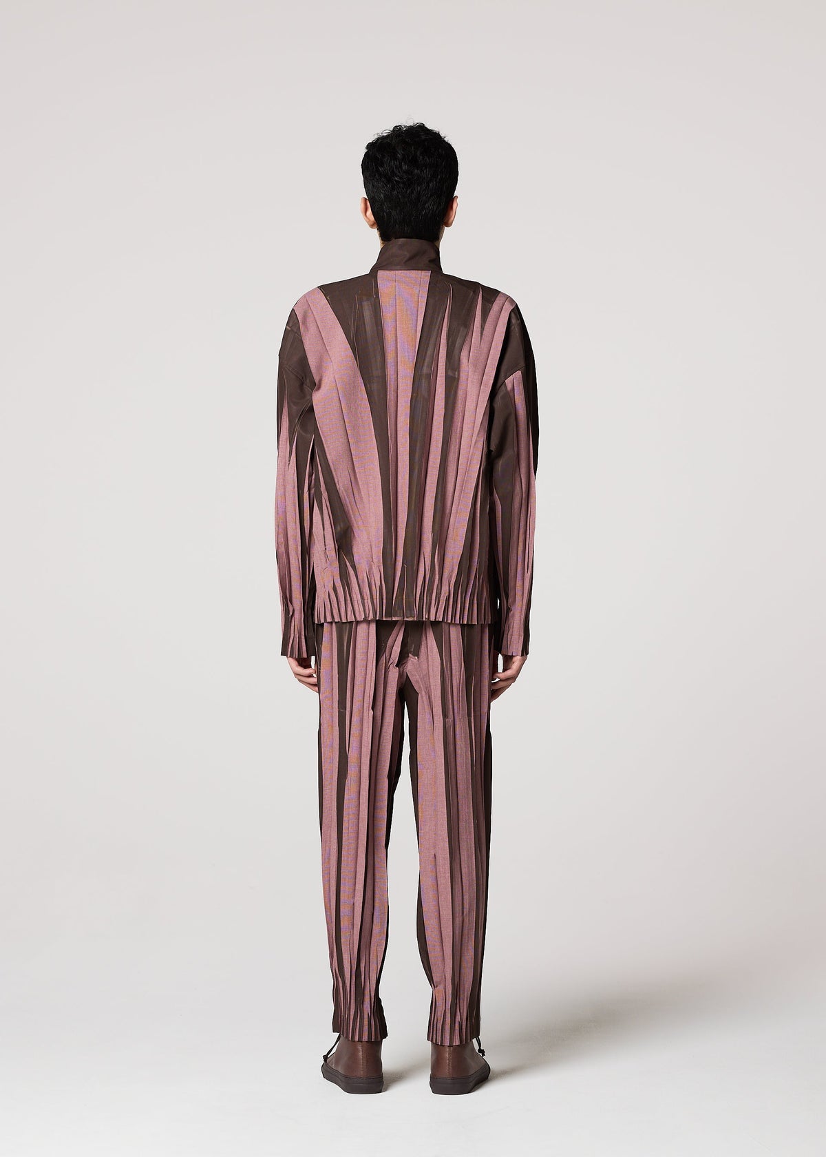 A person faces away, wearing IM MEN's EDGE set—a matching long-sleeve top and ceramic-inspired pants featuring pink and brown vertical abstract stripes—against a plain light background. view 8 of 9