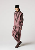 A person models the EDGE set by IM MEN, featuring loose ceramic-inspired pants and a long-sleeved top in muted pink and brown, standing against a plain light background.