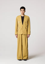 A person faces forward in IM MEN's RESILIENCE, a loose-fitting mustard yellow suit with wide-legged, lightweight wrinkle-resistant pants and a black shirt, set against a plain light background.
