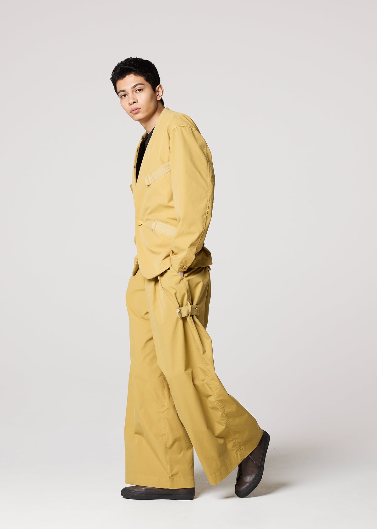 A person models the IM MEN RESILIENCE suit—a loose-fitting mustard yellow ensemble with wide-leg, lightweight, wrinkle-resistant pants and black shoes—posing confidently against a plain light background. view 9 of 9