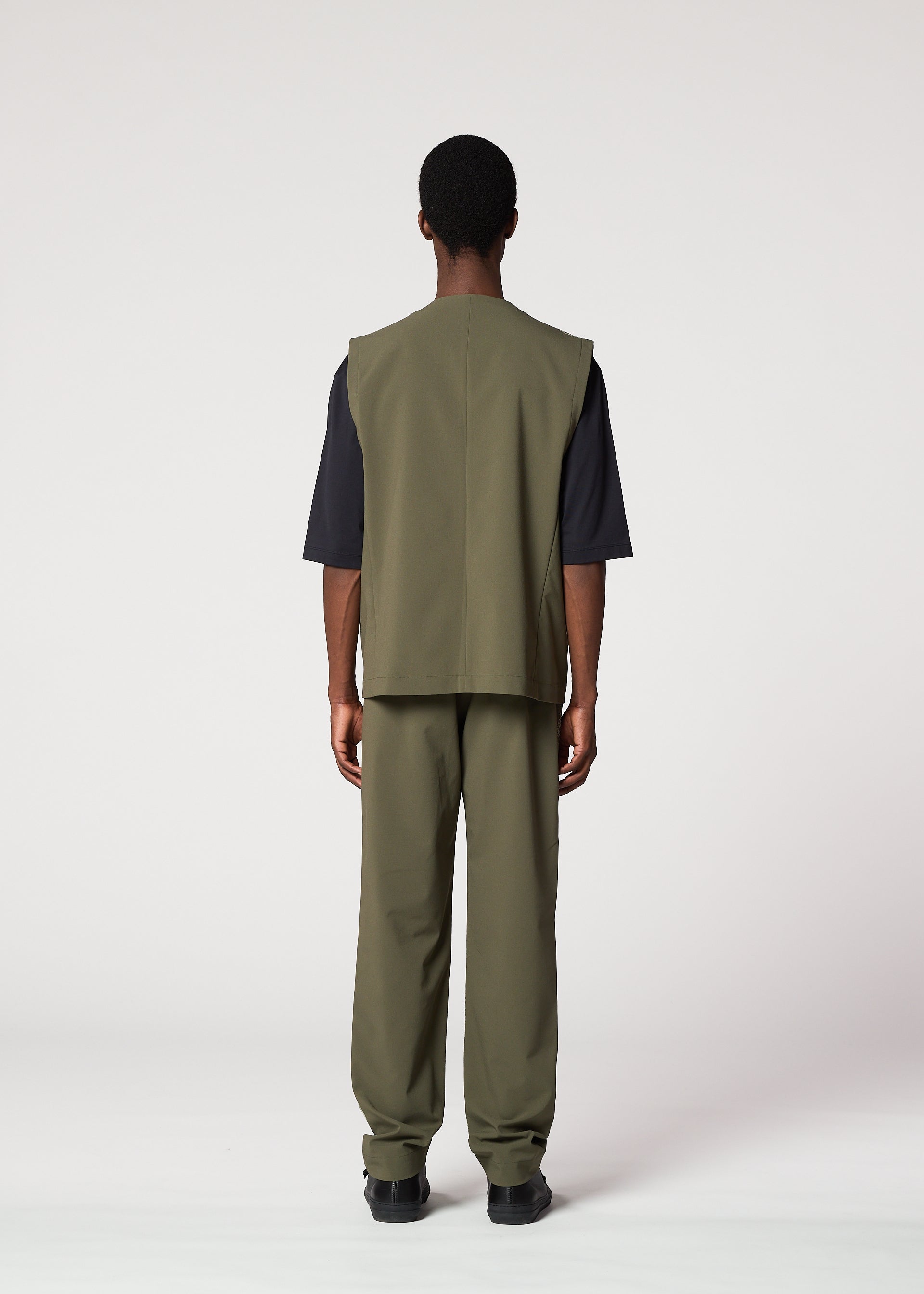 Zoomed view A person faces away from the camera wearing the IM MEN KAIYU suit—olive green sleeveless vest, ash glaze pants, and a short-sleeved black shirt—set against a plain light background.