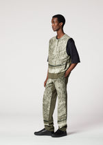 A man models the IM MEN KAIYU sleeveless patterned vest over a black shirt and ash glaze pants with green panels, paired with black shoes. He stands in a studio, facing slightly right against a plain background.