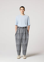 A person with short hair wears IM MEN’s CURVINESS light blue short-sleeve shirt tucked into high-waisted, loose, ceramic artist-inspired black and white striped pants with a belt, paired with white shoes against a plain light gray background.