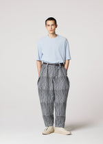A person stands facing forward, wearing IM MEN's CURVINESS light blue t-shirt tucked into high-waisted, loose cotton-linen textured pants with a belt and light shoes against a plain, light background.