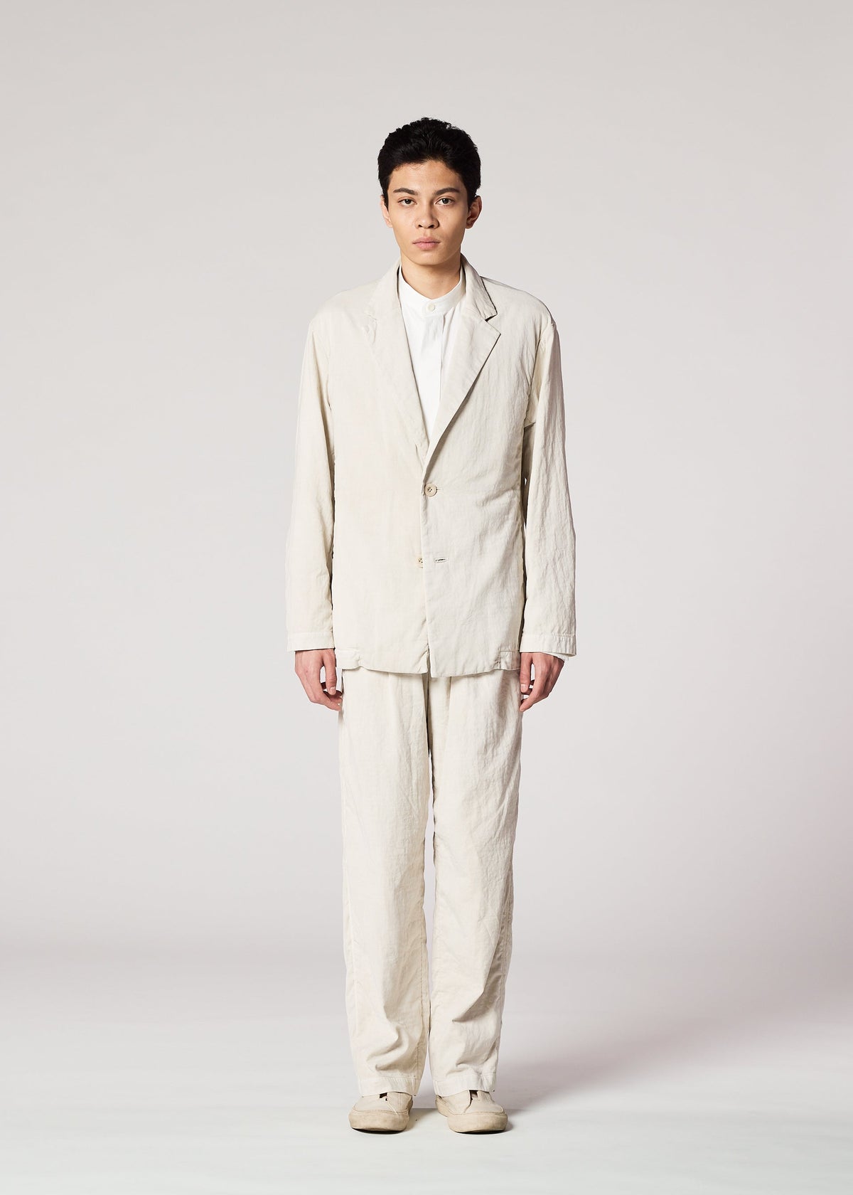 A person stands facing forward, wearing IM MEN’s PIGMENT DOUBLE FACE COTTON cream-colored suit with a soft texture, paired with a white shirt and matching shoes, set against a plain light grey background. view 5 of 8