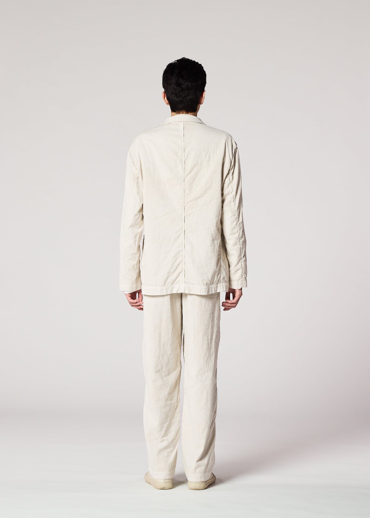 A person faces away from the camera, wearing loose-fitting, cream PIGMENT DOUBLE FACE COTTON clothing by IM MEN with a soft texture, shown against a plain light background. view 7 of 8