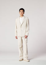 A person faces forward, wearing IM MEN's PIGMENT DOUBLE FACE COTTON loose light beige suit with matching pants, a white shirt underneath, and beige shoes, set against a plain light background.