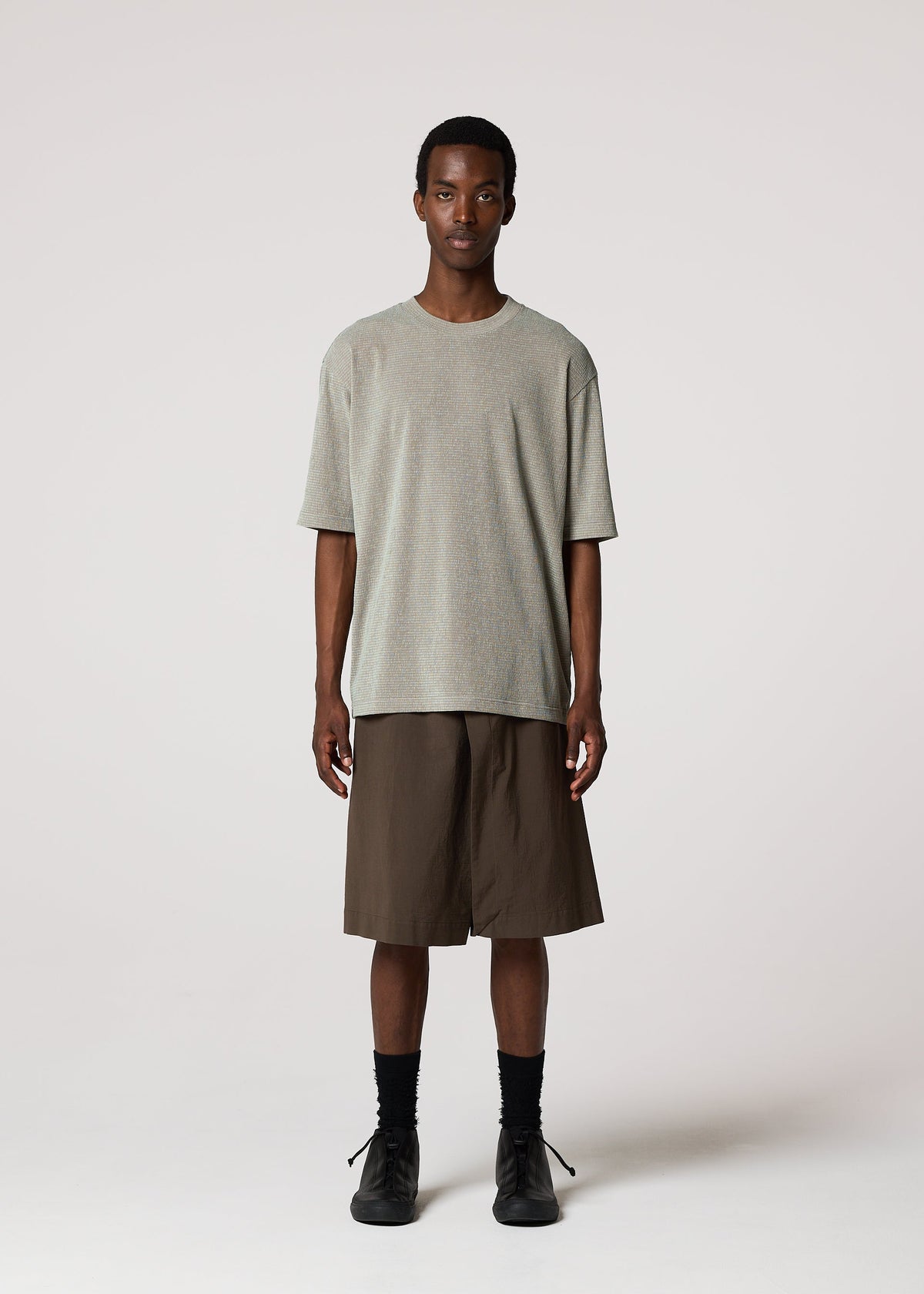 A person faces forward, wearing IM MEN’s NAVY BOTTOMS with a loose light gray t-shirt, black socks, and black shoes against a plain light background. view 6 of 9
