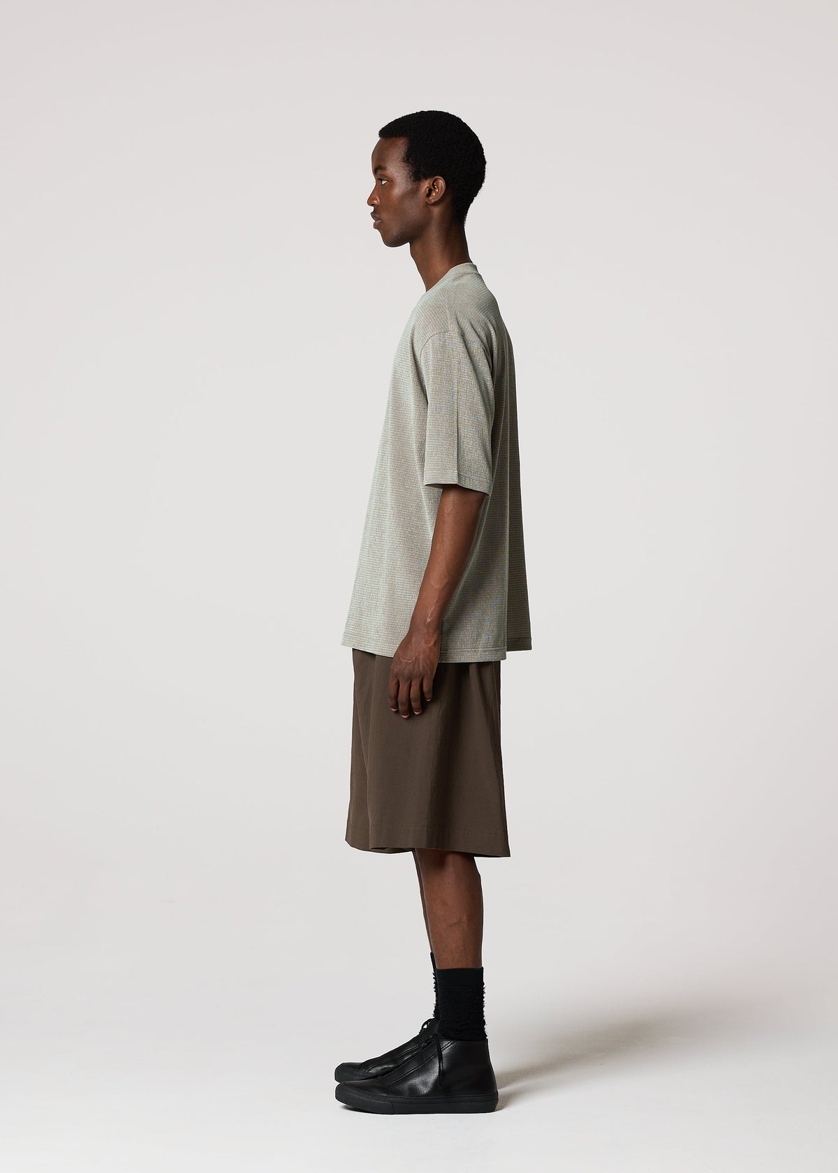A man stands in profile against a white background, wearing a loose gray T-shirt, NAVY BOTTOMS by IM MEN, black socks, and black shoes. view 7 of 9