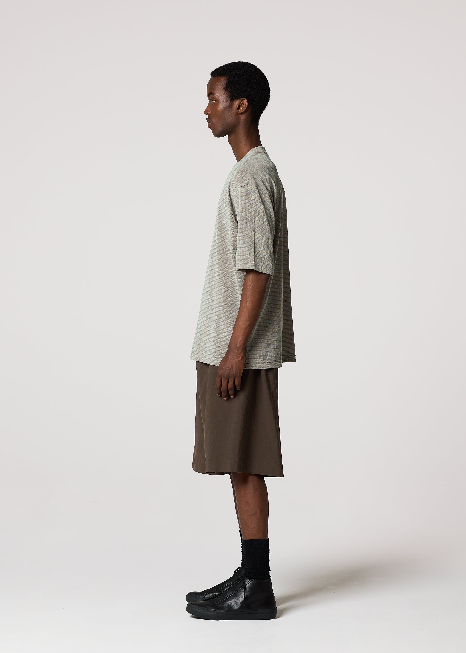 Zoomed view A man stands in profile against a white background, wearing a loose gray T-shirt, NAVY BOTTOMS by IM MEN, black socks, and black shoes.