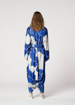 A person with curly hair, facing away, wears the INLAY blue and gray jacquard jumpsuit by IM MEN with a belt and light shoes, set against a plain white background.