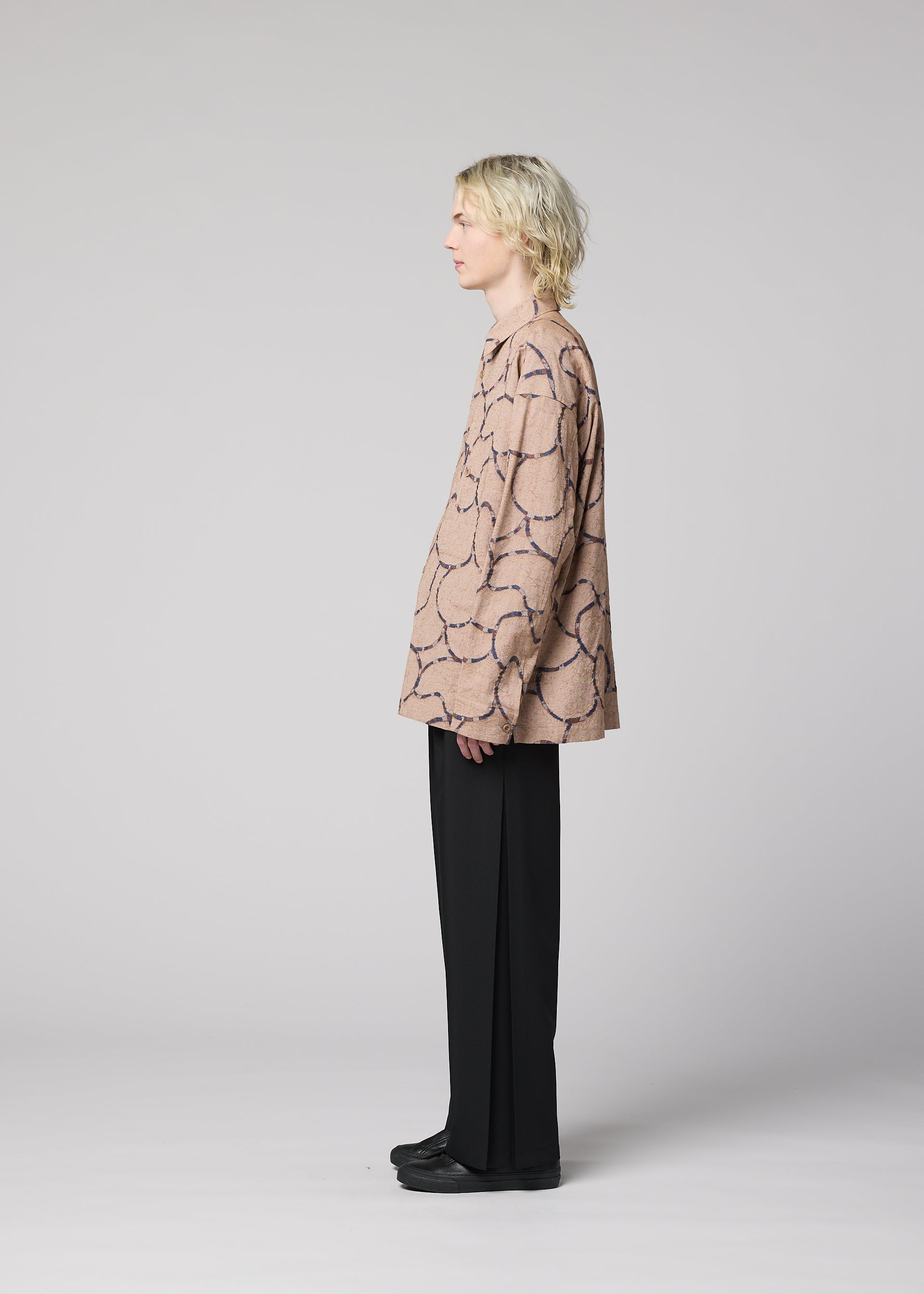 Zoomed view A person with wavy blond hair stands in profile against a light gray background, wearing the IM MEN VASE JACQUARD SHIRT, wide black pants, and black shoes.