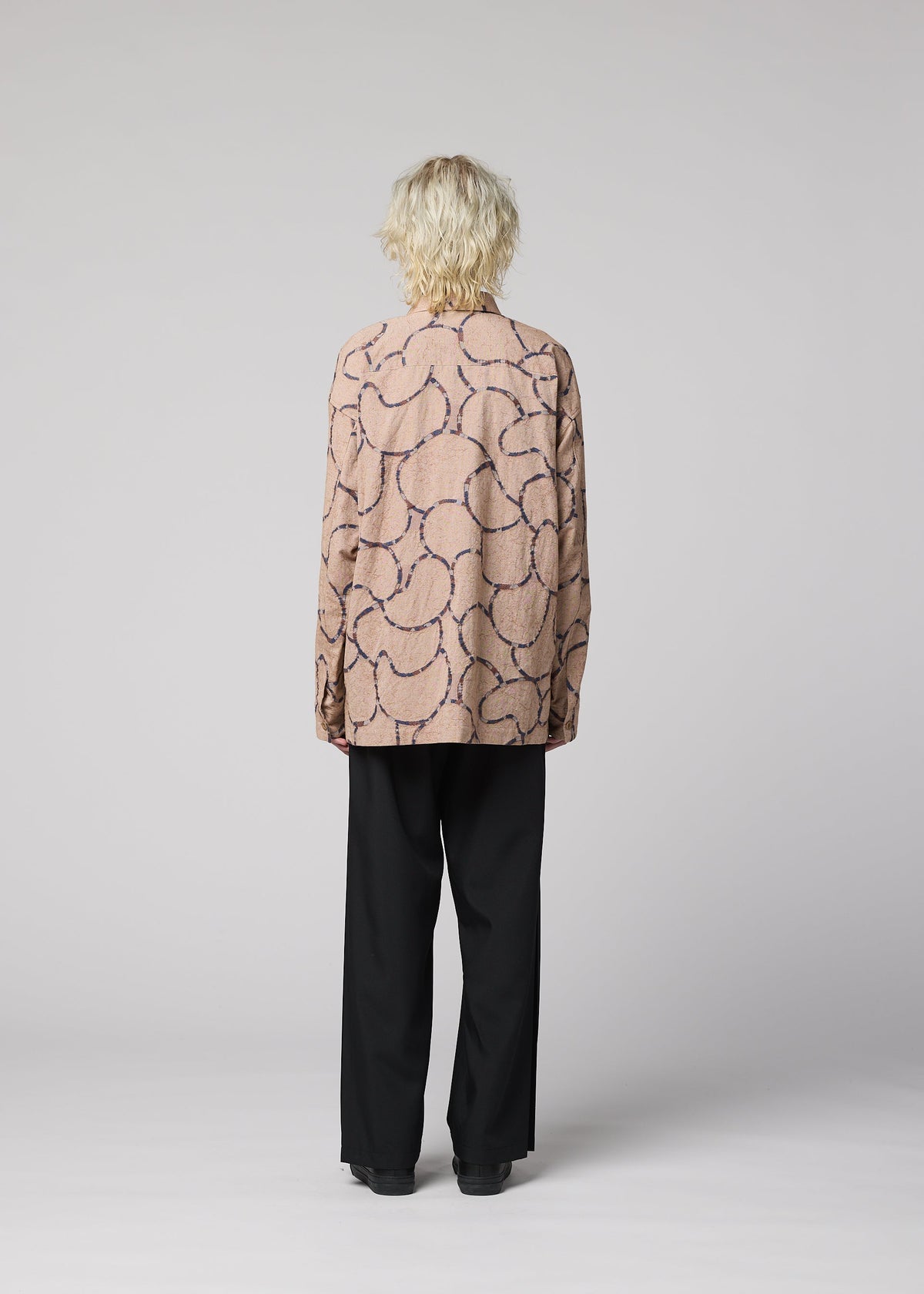 A person with wavy blond hair, seen from behind, wears the IM MEN VASE JACQUARD SHIRT with dark squiggle patterns and black pants, against a plain light gray background. view 6 of 7