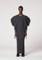 A person stands against a plain background, wearing the IM MEN VASE JACQUARD SHIRT with wide, structured sleeves and circular patterns. They have a calm expression and are wearing black shoes.