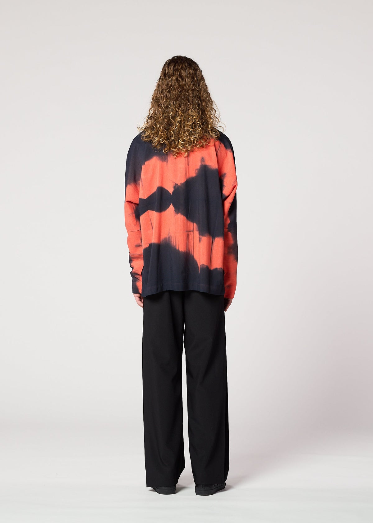 A person with curly hair is seen from behind wearing the IM MEN ITAJIME SHIRT in red and black, paired with black wide-leg pants, against a plain light background. view 8 of 9