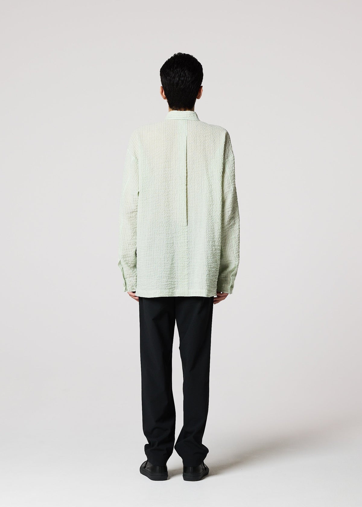 A person faces away from the camera, wearing IM MEN's STRIPE LINEN SHRINK shirt with black pants against a plain light background. view 8 of 9