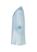 The IM MEN FLOATING LINEN short-sleeved shirt in light blue is shown from the side, featuring a collar and straight hem. Crafted from lightweight linen, it’s displayed on a white background.