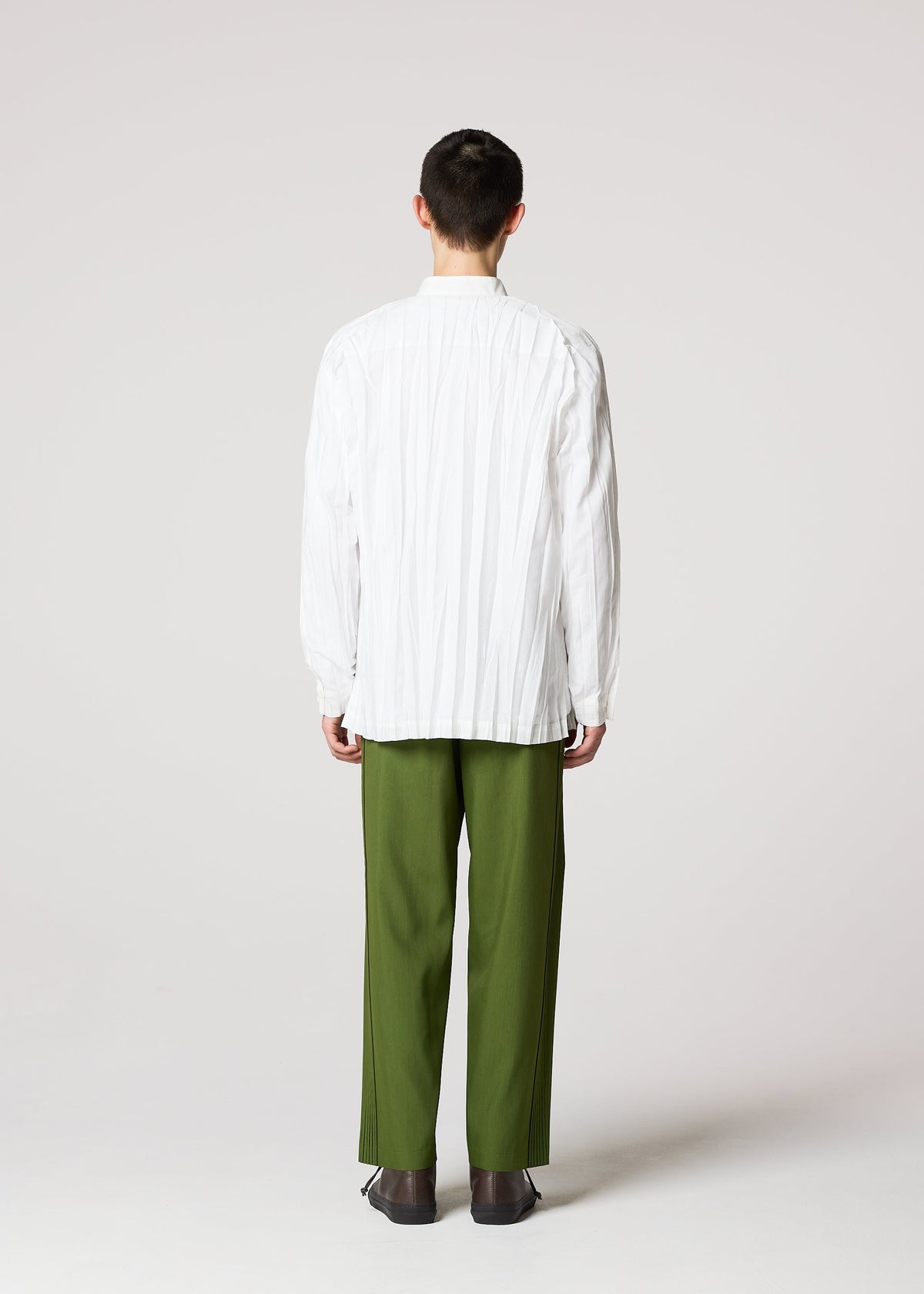 A person faces away from the camera, wearing the IM MEN WRINKLE SHIRT made of recycled polyester with a unique creased finish, paired with olive green pants and dark shoes, set against a plain light gray background. view 8 of 9