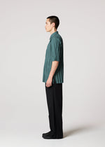 A person with short brown hair stands in profile against a white background, wearing the IM MEN WRINKLE SHIRT in teal recycled polyester, loose black pants, and black shoes.