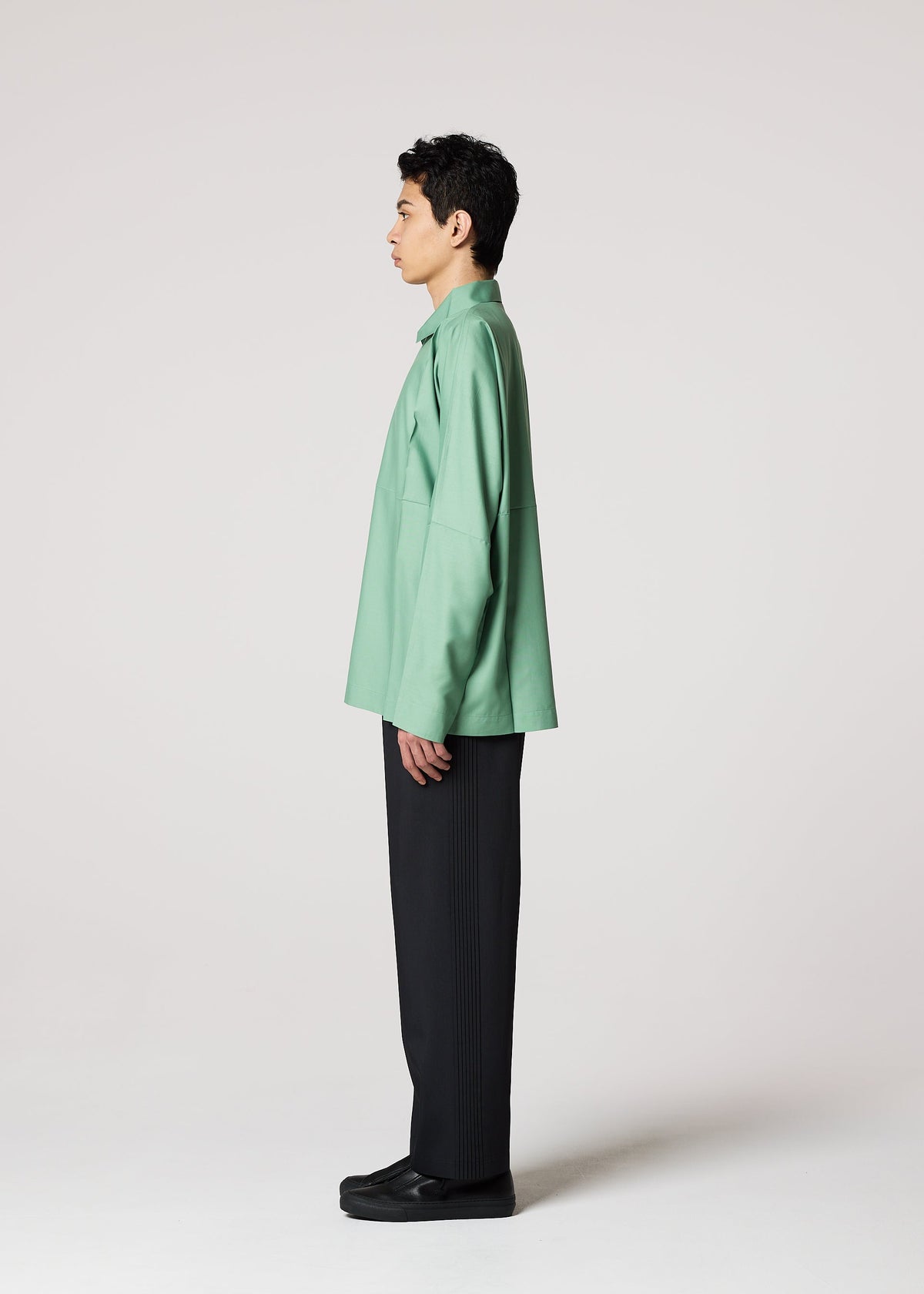 A person in profile faces left, wearing the IM MEN COMPACT SHIRT in green—known for its wrinkle resistance—paired with black pants and shoes, set against a plain light gray background. view 10 of 12