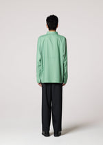 A person with short dark hair, seen from behind against a light gray background, wears the IM MEN COMPACT SHIRT in light green and loose black pants.