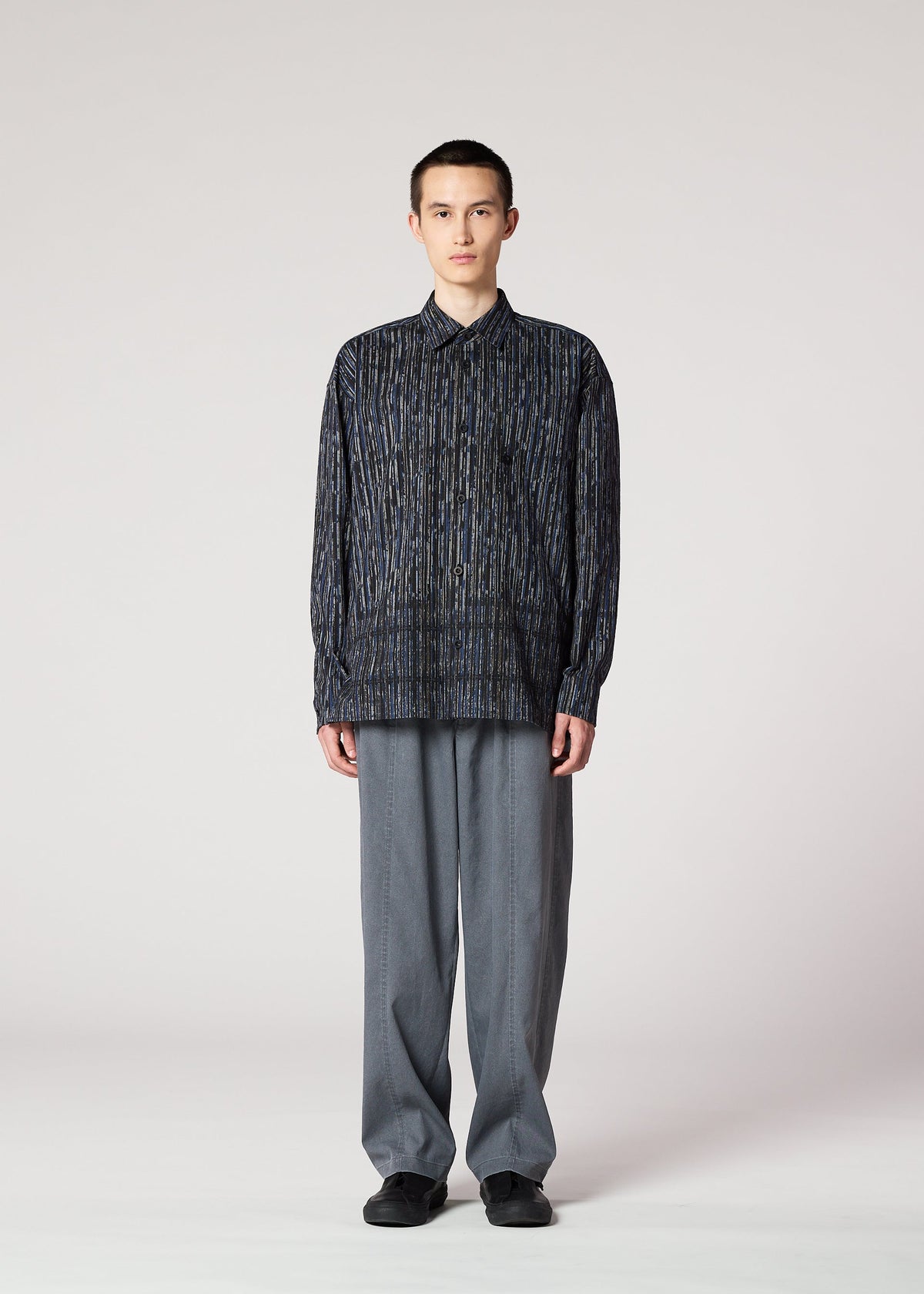 A person stands facing forward against a plain light background, wearing the IM MEN CURVINESS SHIRT inspired by Shoji Kamoda, paired with loose-fitting gray pants and black shoes. view 5 of 8